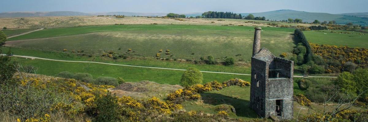 A picture of a moorland view. In the foreground there is a ruined old stone building, in the background is rolling fields and a blue sky.