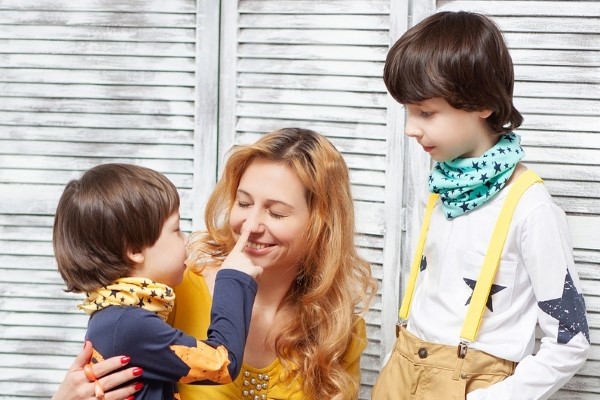 On the left a young child with a yellow neckerchief with starts on pokes a woman in the middle on the nose. A slightly older boy wearing suspenders and a white top with blue starts on watches on