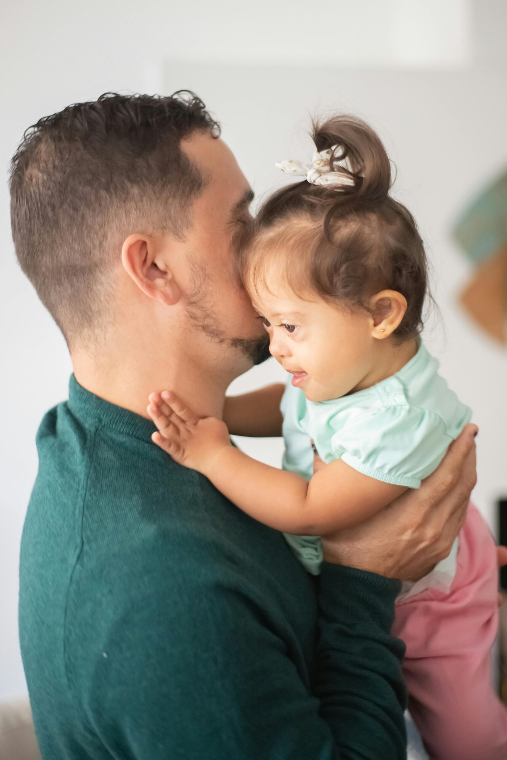 A man in a dark green top lifts up a young girl who is wearing pink shorts and has a light blue top on.