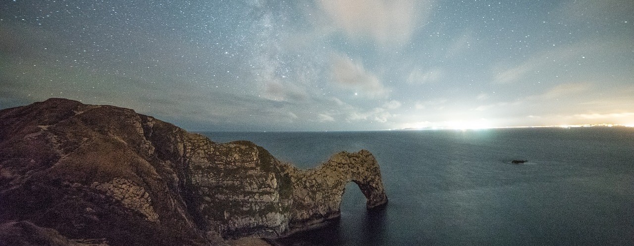 This image shows durdle door in Dorset, a famous rock formation at night. In the background you can see the sun setting.